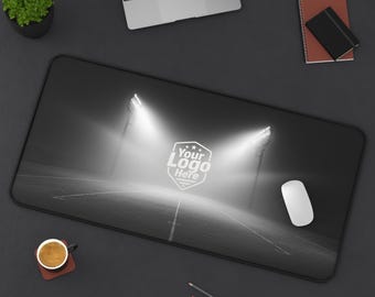 Peut inclure: Tapis de souris rectangulaire noir et blanc représentant une scène de stade avec des projecteurs lumineux et le texte "Your Logo Here". Une souris blanche, un ordinateur portable, des crayons et une tasse de café sont sur une surface sombre.