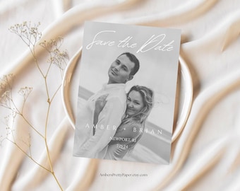 Puede incluir: Una tarjeta de invitación de boda en blanco y negro con una pareja en la playa. La tarjeta incluye el texto "Save the Date" en una elegante escritura, junto con los nombres Amber y Brian, la ubicación Newport, RI, y la fecha 15/07/24.