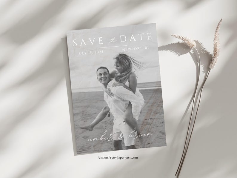 Puede incluir: Tarjeta de guardar la fecha en blanco y negro con una pareja en la playa. El texto dice "Save the Date" con la fecha "July 15, 2023" y la ubicaci&oacute;n "Newport, RI". Los nombres de la pareja est&aacute;n escritos en cursiva debajo de la foto: "amber & brian".