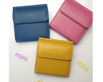 May include: Three small, square wallets in blue, pink, and yellow. Each wallet has a flap closure and a textured surface. The word "mini" is written in purple and green around the wallets.