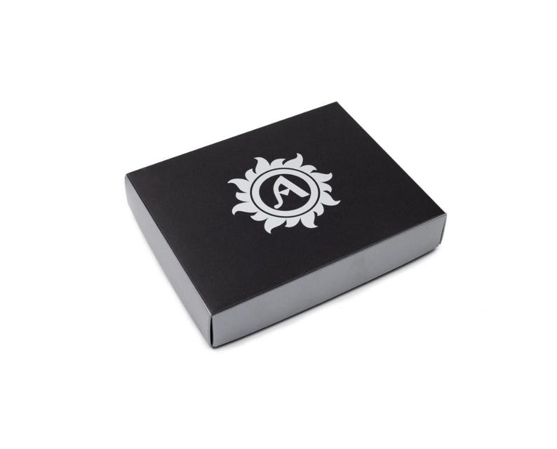 A black box with a silver rim and a white logo on the top. The logo is a sunburst design with the letter "A" in the center. The box is square and sits on a white background.