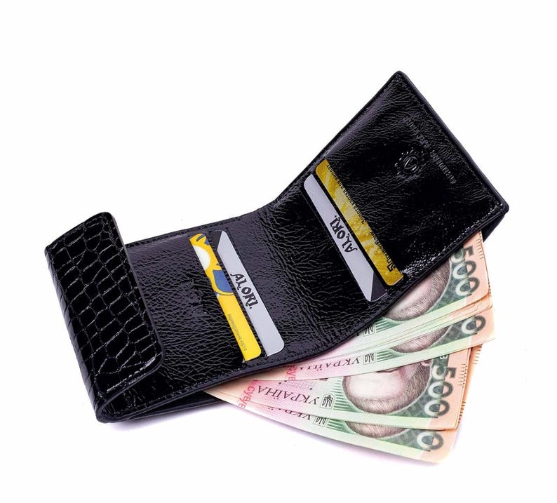 Black leather wallet with a crocodile texture on the flap. The wallet is open, revealing several credit cards and  banknotes.