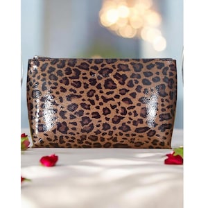 May include: A rectangular cosmetic bag with a brown leopard print pattern. The bag has a zipper closure and a glossy finish. The bag is sitting on a white surface.