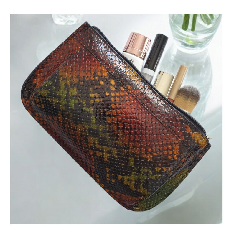 Multi coloured snake print makeup bag with a zipper closure. The bag is open and filled with various makeup items, including a bottle of lotion, a tube of mascara, and makeup brushes.
