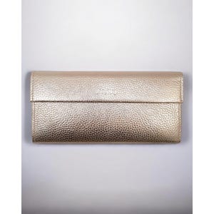 Könnte beinhalten: Eine goldfarbene Geldbörse mit strukturierter Oberfläche. Die rechteckige Geldbörse hat einen Klappverschluss. Das Wort "AMISU" ist auf der Vorderseite sichtbar. Die Geldbörse scheint aus Leder zu sein.