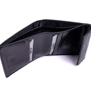 Black leather wallet with a textured exterior. The wallet is open, revealing card slots and the interior lining. The brand name is visible on the inside. The wallet is designed to hold cards and cash.