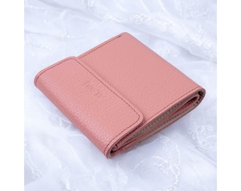 May include: A dusty rose pink bi-fold wallet with a textured pebbled surface. The wallet features a rectangular flap closure on the front with the word ALON embossed in small capital letters. The edges are finished with matching tonal stitching.