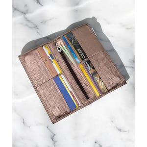 May include: Open, rose-gold colored wallet with multiple card slots and a zippered compartment. The wallet is filled with various credit cards and identification cards. The wallet is rectangular and made of textured material.
