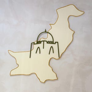 May include: A cream-colored map of Pakistan with a gold outline. A green outline of a building is superimposed on the map. The background is a textured, off-white surface.