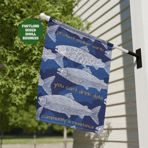 May include: A rectangular garden flag featuring a dark blue background with a repeating pattern of white line-art fish. The text reads: protect mother earth, you can't drink data, and community is resistance in orange lettering on the flag.