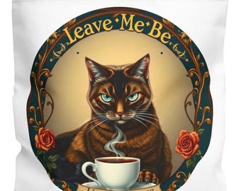 May include: A white tote bag with a round, green and gold design featuring a brown tabby cat with green eyes. The cat is holding a white coffee cup with steam rising from it. The design also includes roses and the text "Leave Me Be. Until Cup Three."