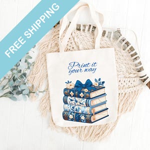 May include: A white canvas tote bag with blue and white floral patterned books stacked on top of each other. A blue bow is tied around the top book. The text "Print it your way" is printed on the bag.