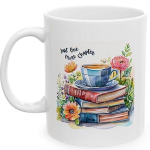 Könnte beinhalten: Weiße Keramiktasse mit einer Aquarell-Illustration einer Tasse Tee, einem Stapel Bücher und Blumen. Der Text "Just One More Chapter" ist auf die Tasse gedruckt.