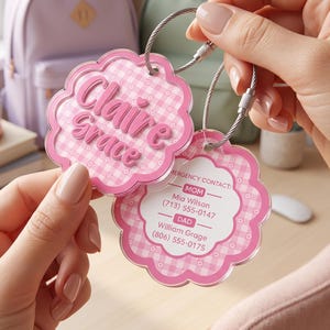 May include: Two scalloped, pink and white gingham acrylic bag tags attached to a silver wire ring. One tag features the name Claire Grace in pink script. The other tag displays emergency contact information for Mom and Dad with phone numbers.