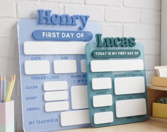 May include: Two rectangular acrylic signs for tracking school milestones. The larger light blue sign features the name Henry and fields for date, age, and interests. The smaller teal sign features the name Lucas and fields for date, height, and age.