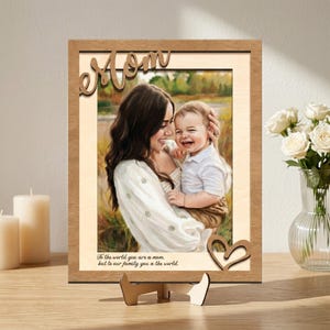 Puede incluir: Foto enmarcada en madera con una imagen de una madre y un niño. La palabra "Mom" está recortada en madera en la parte superior. Un corazón de madera está en la parte inferior derecha. El texto dice: "Para el mundo eres una mamá, pero para nuestra familia eres el mundo."