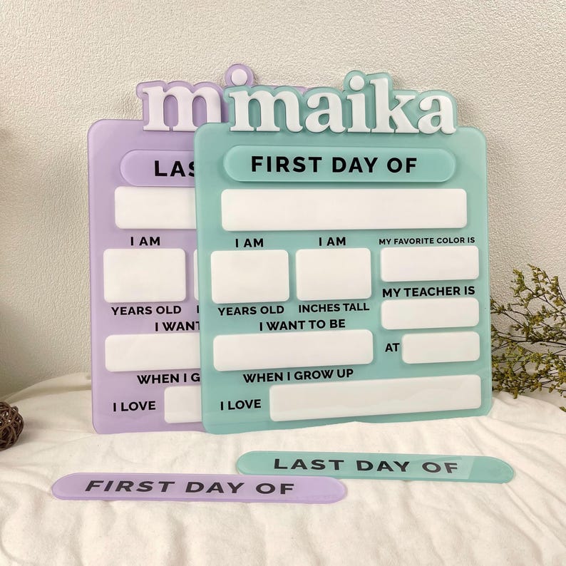 May include: A light purple and a light green acrylic sign set featuring the name maika in white 3D lettering. The signs include blank white rectangular spaces for writing details like age, height, favorite color, teacher, and future career goals.