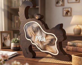 May include: A dark brown wooden cat-shaped shadow box with a clear front panel. The name Miu is printed in white script on the glass. The interior contains light-colored fur, and a small wooden heart with a paw print sits on the cat's back.