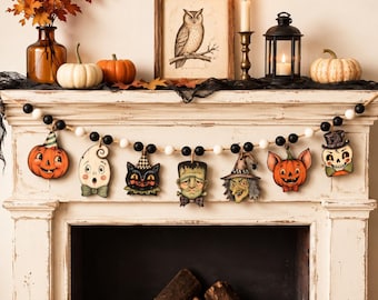 May include: A Halloween-themed garland featuring alternating black and white wooden beads strung on twine, with seven hanging wooden cutouts depicting a pumpkin, ghost, black cat, Frankenstein's monster, witch, bat-eared pumpkin, and a skull.