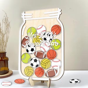 May include: A wooden jar-shaped reward chart with a white outline, filled with colorful sports balls. The text "Mrs. Buck's Reward Jar" is displayed in the center. Includes baseball, basketball, soccer, football, and tennis ball designs.