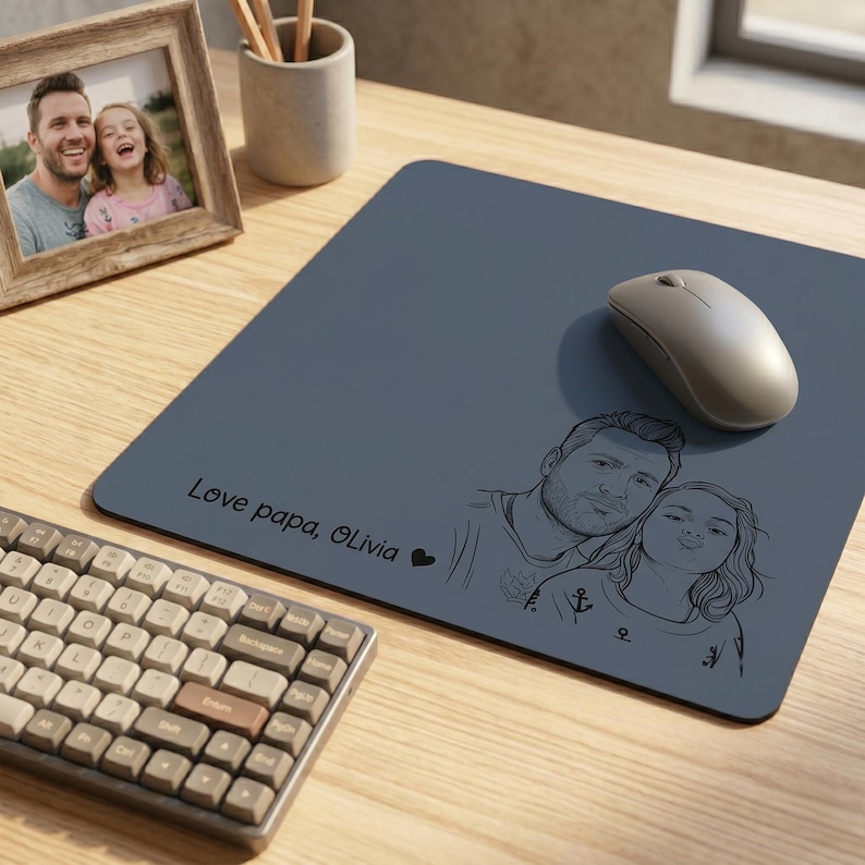 Peut inclure: Tapis de souris gris avec un croquis d'un p&egrave;re et de sa fille, le texte "Love papa, Olivia" et un c&oelig;ur. Une souris sans fil est pos&eacute;e sur le tapis. Une photo encadr&eacute;e et un clavier sont &eacute;galement visibles.