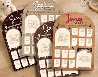 May include: Four wooden baby milestone boards with arched tops. Each board has a photo frame, the words "Hello World" and "New Born". One board says "Happy Birthday" and "One Year". The boards are in shades of brown.