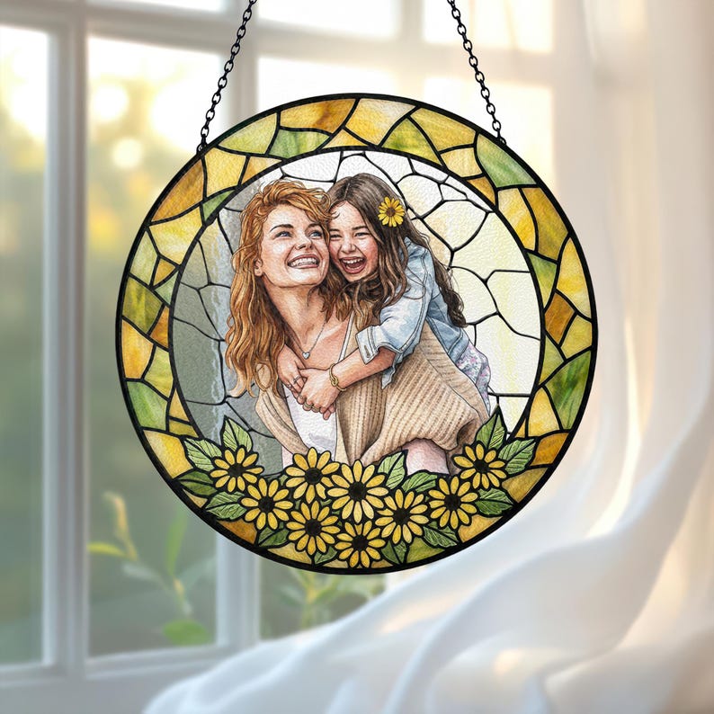 May include: Round stained glass window art featuring a mother and child embracing, surrounded by sunflowers. The artwork is framed with a black metal chain and a yellow and green stained glass border. The image depicts a joyful moment.