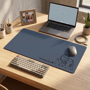 Peut inclure: Un tapis de bureau bleu avec une illustration personnalis&eacute;e d'un couple et le texte "Love papa, Olivia". Un ordinateur portable, un clavier et une souris sont sur le bureau en bois. Une photo encadr&eacute;e et une plante en pot sont &eacute;galement visibles.