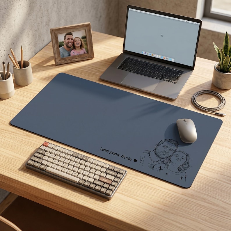 Peut inclure: Un tapis de bureau bleu avec une illustration personnalis&eacute;e d'un couple et le texte "Love papa, Olivia". Un ordinateur portable, un clavier et une souris sont sur le bureau en bois. Une photo encadr&eacute;e et une plante en pot sont &eacute;galement visibles.