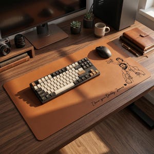 Peut inclure: Un tapis de bureau en cuir marron avec un clavier noir et blanc, une souris et un dessin d'un p&egrave;re et d'un enfant. Le texte "I love you Daddy James" est imprim&eacute; sur le tapis.