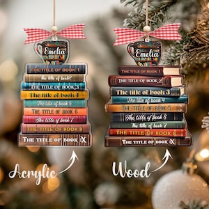 May include: Two Christmas tree ornaments depicting stacks of books, each with a coffee cup and a red and white gingham bow. One is acrylic, the other wood. The books are labelled with titles and the name "Emelia".