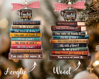 Puede incluir: Dos adornos navideños con forma de pilas de libros, cada uno con una taza de café y un lazo a cuadros rojos y blancos. Uno es de acrílico, el otro de madera. Los libros están etiquetados con títulos y el nombre "Emelia".