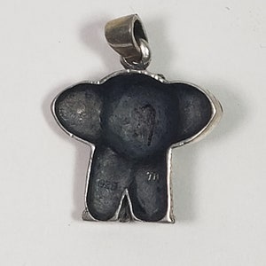May include: A silver pendant in the shape of an elephant, with a dark gray body and large ears. The pendant has a loop at the top for a chain. The back of the pendant has the markings "1925" and "7H".