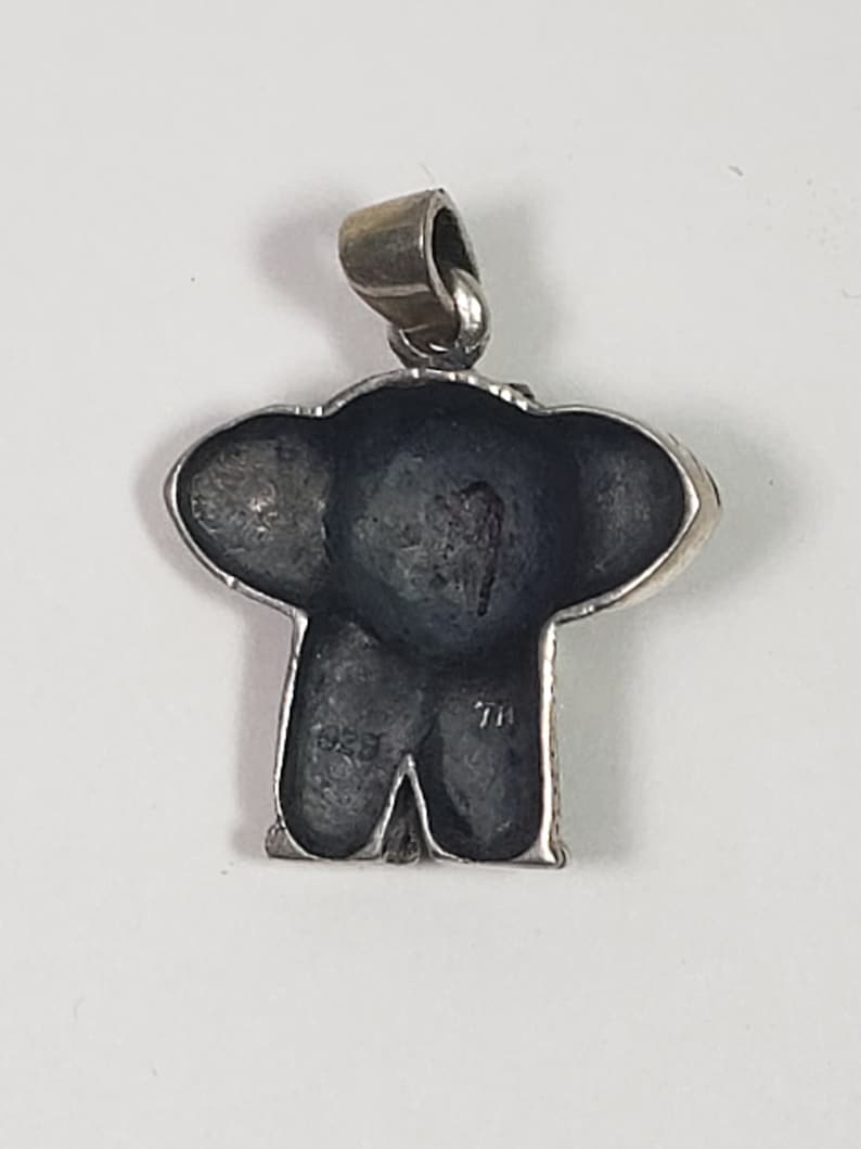 May include: A silver pendant in the shape of an elephant, with a dark gray body and large ears. The pendant has a loop at the top for a chain. The back of the pendant has the markings "1925" and "7H".