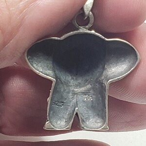 May include: A silver pendant in the shape of a teddy bear. The pendant has a loop at the top for a chain. The back of the pendant is stamped with "925". The bear's body is detailed with textured silver.