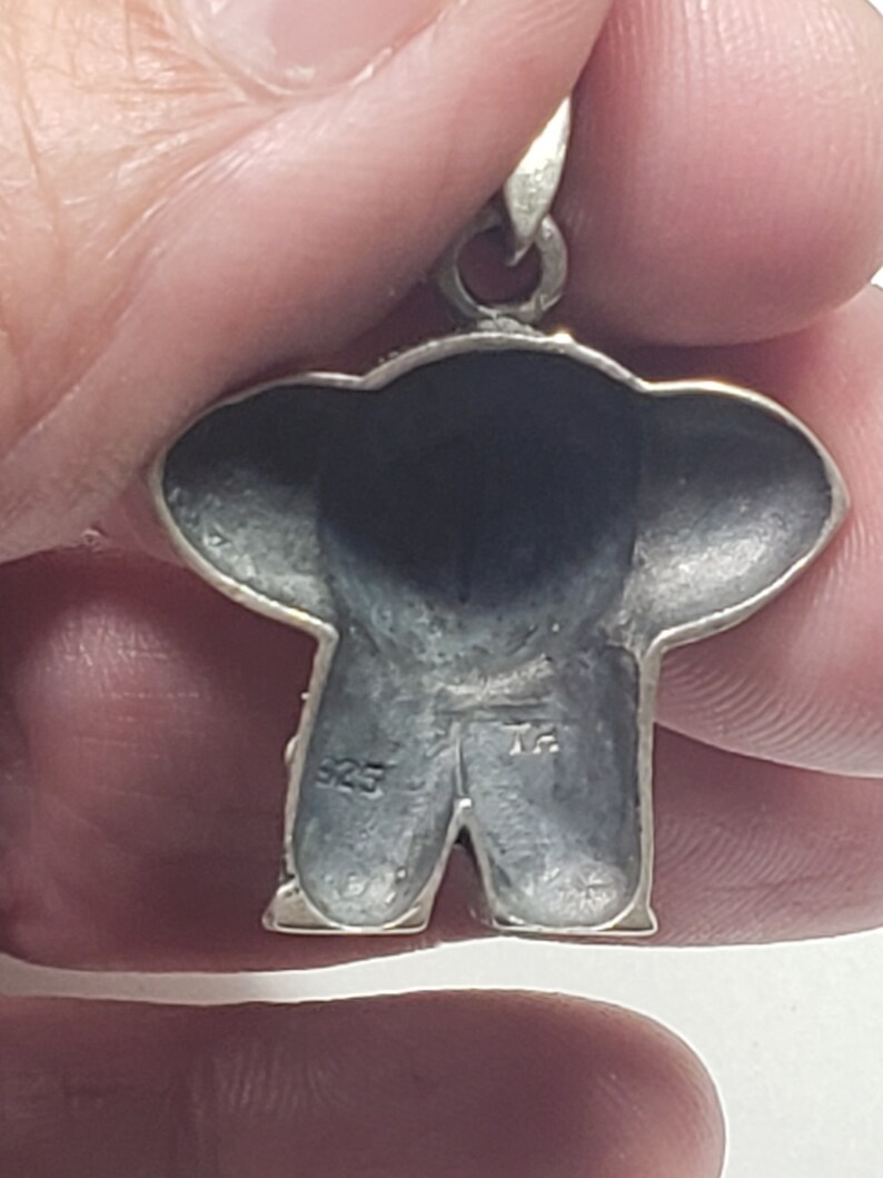 May include: A silver pendant in the shape of a teddy bear. The pendant has a loop at the top for a chain. The back of the pendant is stamped with "925". The bear's body is detailed with textured silver.