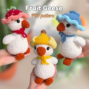 May include: Three handmade crochet geese with fruit-themed hats. One wears a strawberry hat, another a blueberry hat, and the third a lemon hat. The geese have orange beaks and feet, and white bodies. The text "Fruit Geese PDF pattern" is visible.