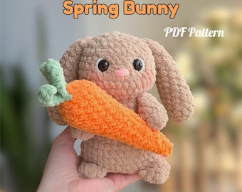 May include: A plush, light brown bunny holding an orange carrot with green leaves. The bunny has black eyes and a pink nose. Text on the image reads "Spring Bunny" and "PDF Pattern". The words "No sew!" are also visible.