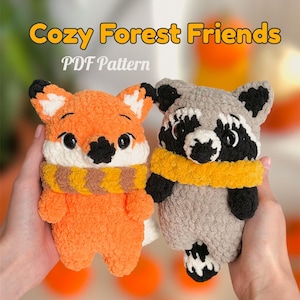 May include: Two handmade plush forest animal toys: an orange fox and a grey raccoon. The fox has a white and brown scarf, and the raccoon has a yellow scarf. The text "Cozy Forest Friends PDF Pattern" is at the top of the image.