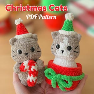 以下が含まれることがあります： サンタ帽をかぶった、グレーとグレーと白の2匹のかぎ針編みの猫の置物。1匹の猫はキャンディケインを持ち、もう1匹は緑のリボンが付いた赤いギフトボックスに入っています。「Christmas Cats PDF Pattern」というテキストが上部にあります。