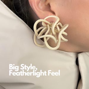 May include: An off-white, textured, sculptural earring featuring a complex, interconnected series of loops and curves. The text "Big Style, Featherlight Feel" is printed in white in the lower left corner of the image.