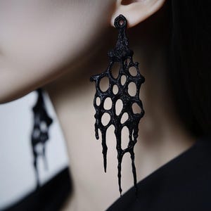 May include: A pair of black, dripping, honeycomb-shaped earrings. The earrings are made of a textured, 3D printed material.