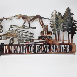 May include: Metal wall art featuring a truck, excavator, and trees, with mountains in the background. The text "IN MEMORY OF FRANK SLYTER" is displayed at the bottom. The artwork is made of brown and copper-toned metal.