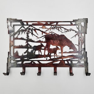 May include: Metal key rack with a silhouette of a mountain range and three deer. The rack has five hooks and a rustic brown finish.