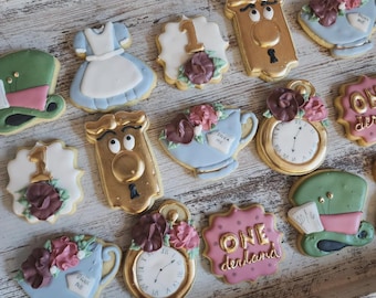 May include: A collection of Alice in Wonderland themed sugar cookies decorated with royal icing. The cookies feature characters like the Mad Hatter, the Queen of Hearts, and the Cheshire Cat. Some cookies have the number "1" and the phrase "One derland" on them.