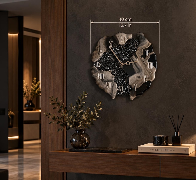 May include: A circular wall clock with an irregular, organic edge measuring 15.7 inches in diameter. The clock face features a central section of black textured material, surrounded by swirling gray and black resin, with gold Roman numerals and hands.