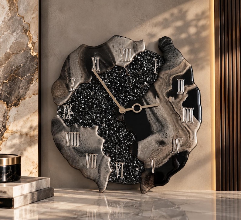 May include: A wall clock with an irregular, organic shape featuring a black and silver marbled resin border. The center contains a textured, dark crystalline surface with silver Roman numerals and thin, gold-colored metal clock hands.