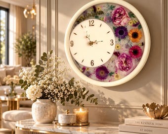 May include: A round wall clock with a white frame and a white face featuring black numerals at 3, 6, 9, and 12. The right side of the clock is filled with a variety of pressed, colorful flowers including pink, purple, and orange blossoms.