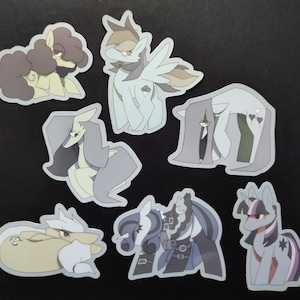 Könnte beinhalten: Eine Sammlung von sieben Cartoon-Pony-Aufklebern in verschiedenen Posen und Farben. Die Aufkleber zeigen Ponys mit unterschiedlichen Mähnen, Schwänzen und Markierungen in Grau-, Blau- und Brauntönen. Einige haben Flügel oder dekorative Elemente.