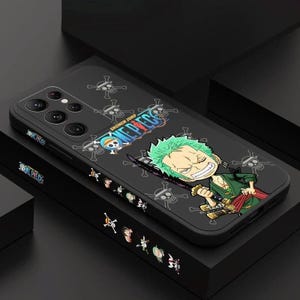 May include: Black phone case featuring a colorful illustration of a character from the anime series "One Piece." The case has the series' logo and the character Zoro with green hair and holding a sword. The case is on a black surface.